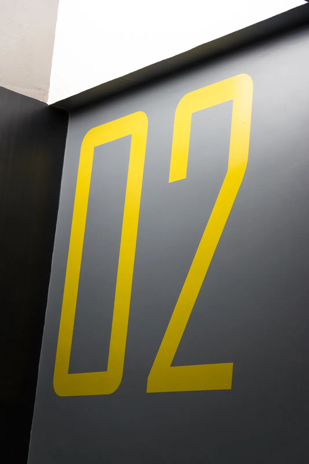 O número 02 pintado em amarelo numa parede cinza da garagem.