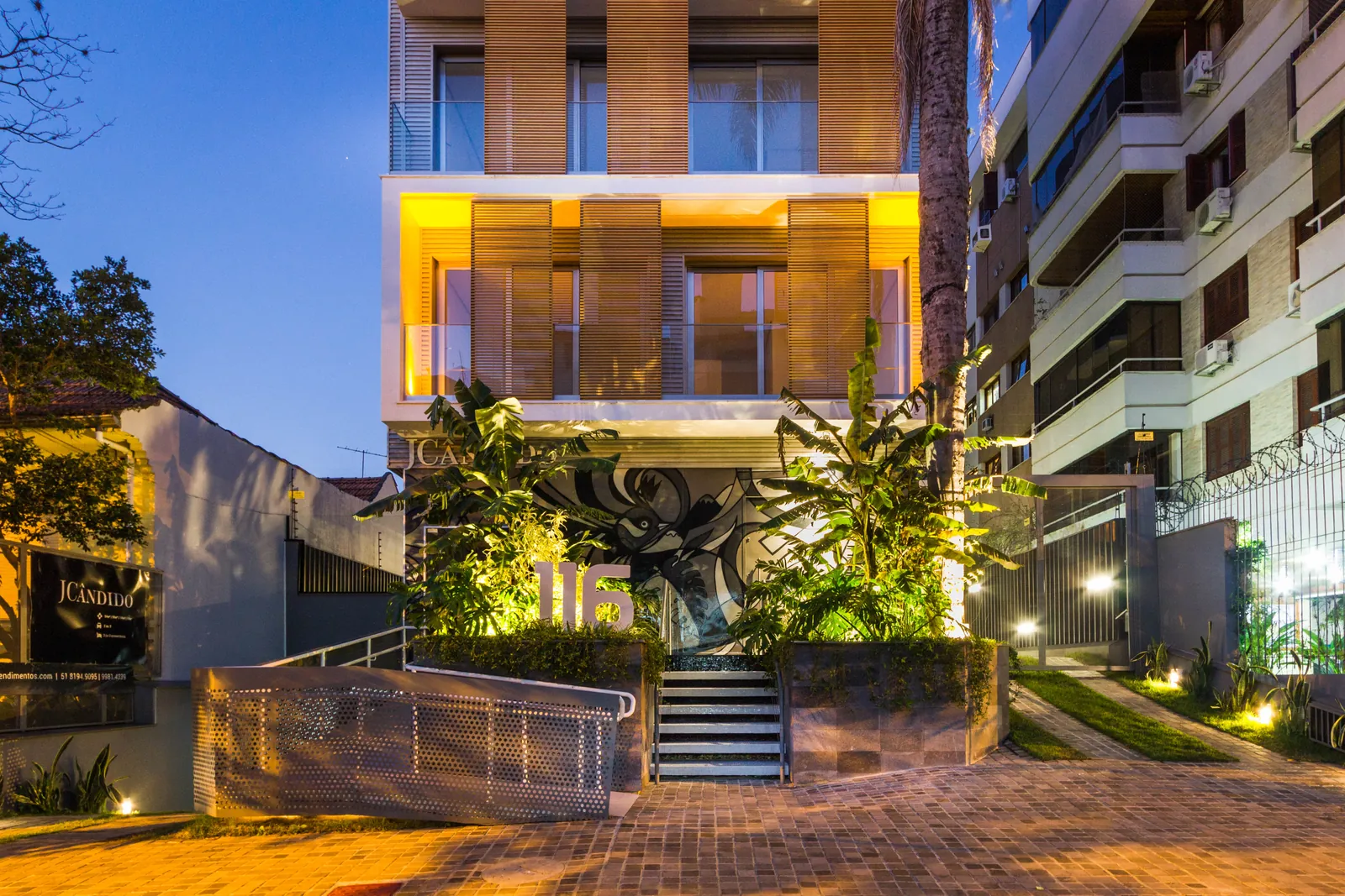 A entrada do Edifício JCândido à noite, com o jardim e os painéis iluminados.