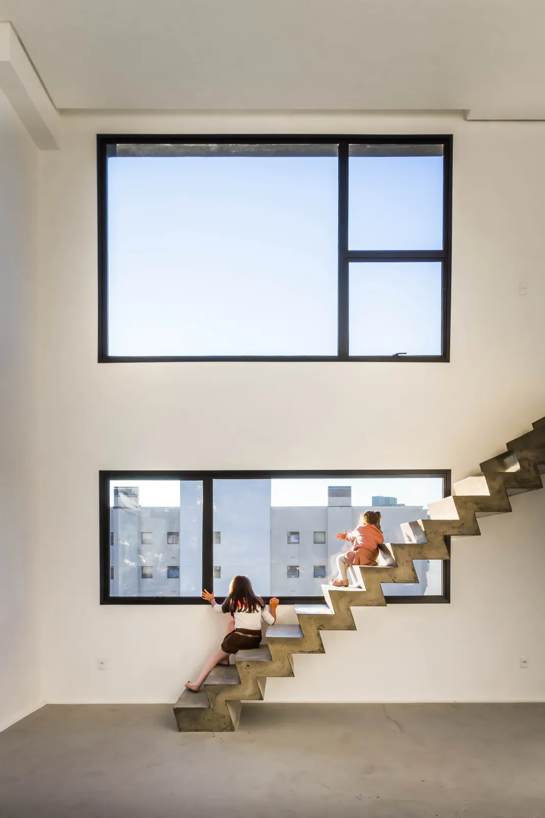 Interior com pé-direito duplo, janelas grandes e uma escada de degraus presos na parede.