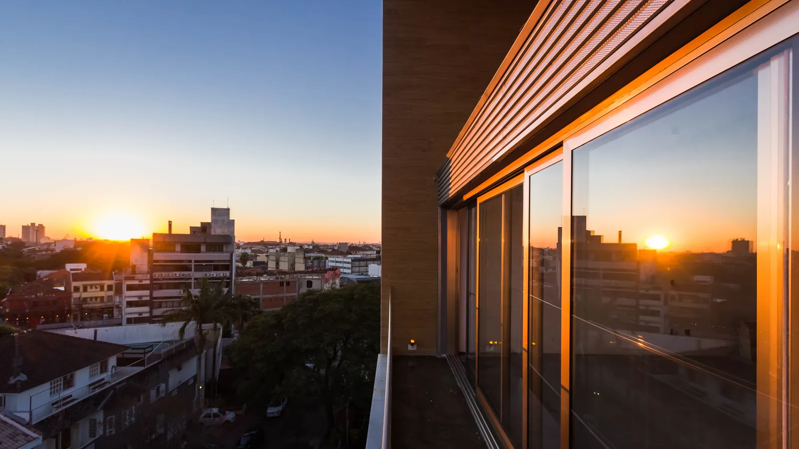 O pôr do sol sobre Porto Alegre refletido no vidro de uma varanda.