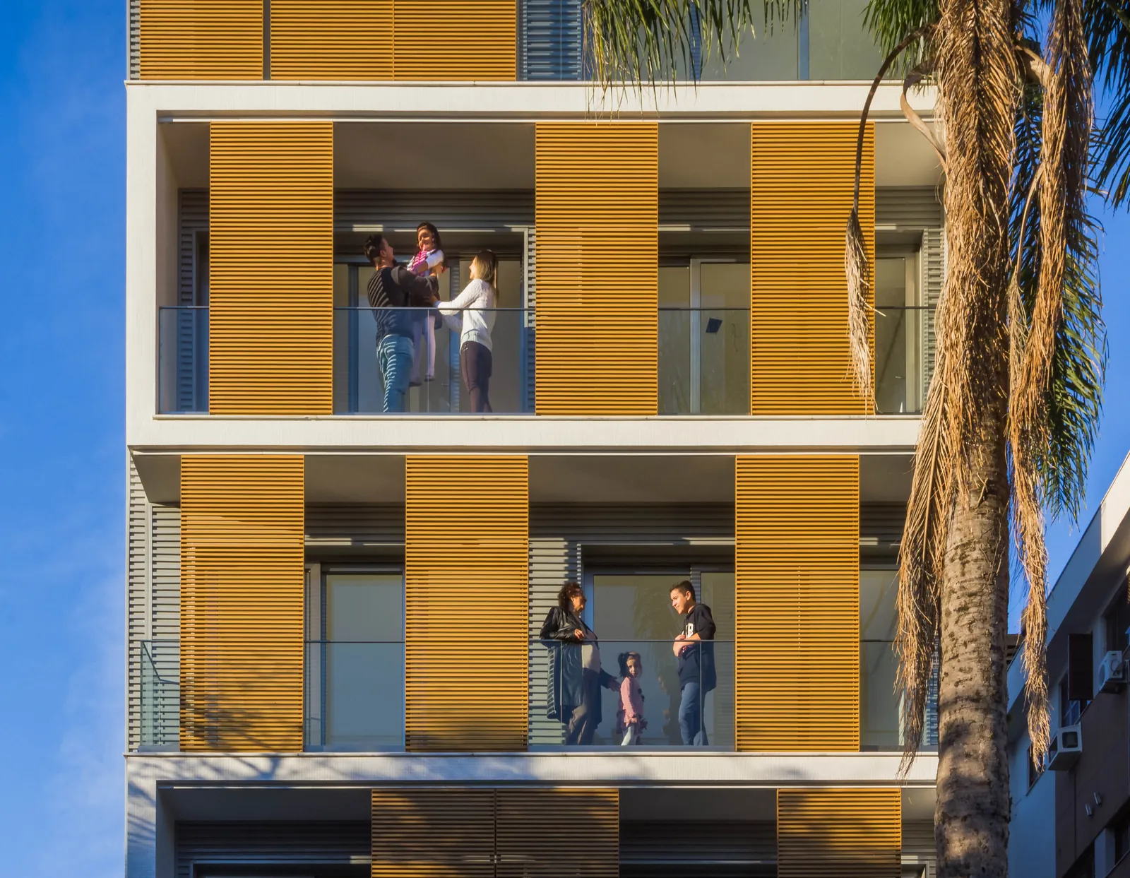 Moradores nas varandas entre os painéis de madeira da fachada.