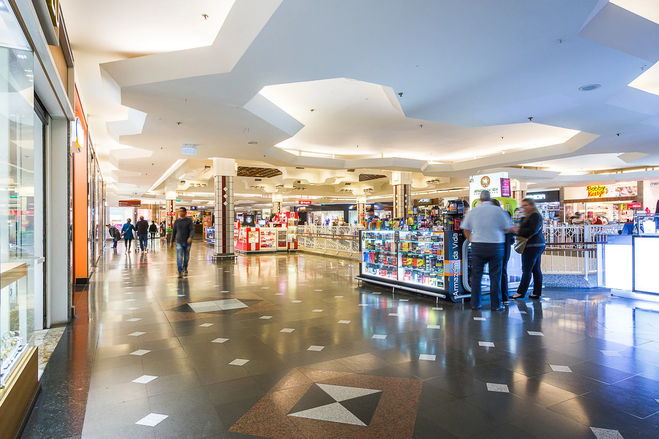 Galeria do Bourbon Shopping Ipiranga, com piso de pedra, quiosques, lojas ao fundo e teto recortado.