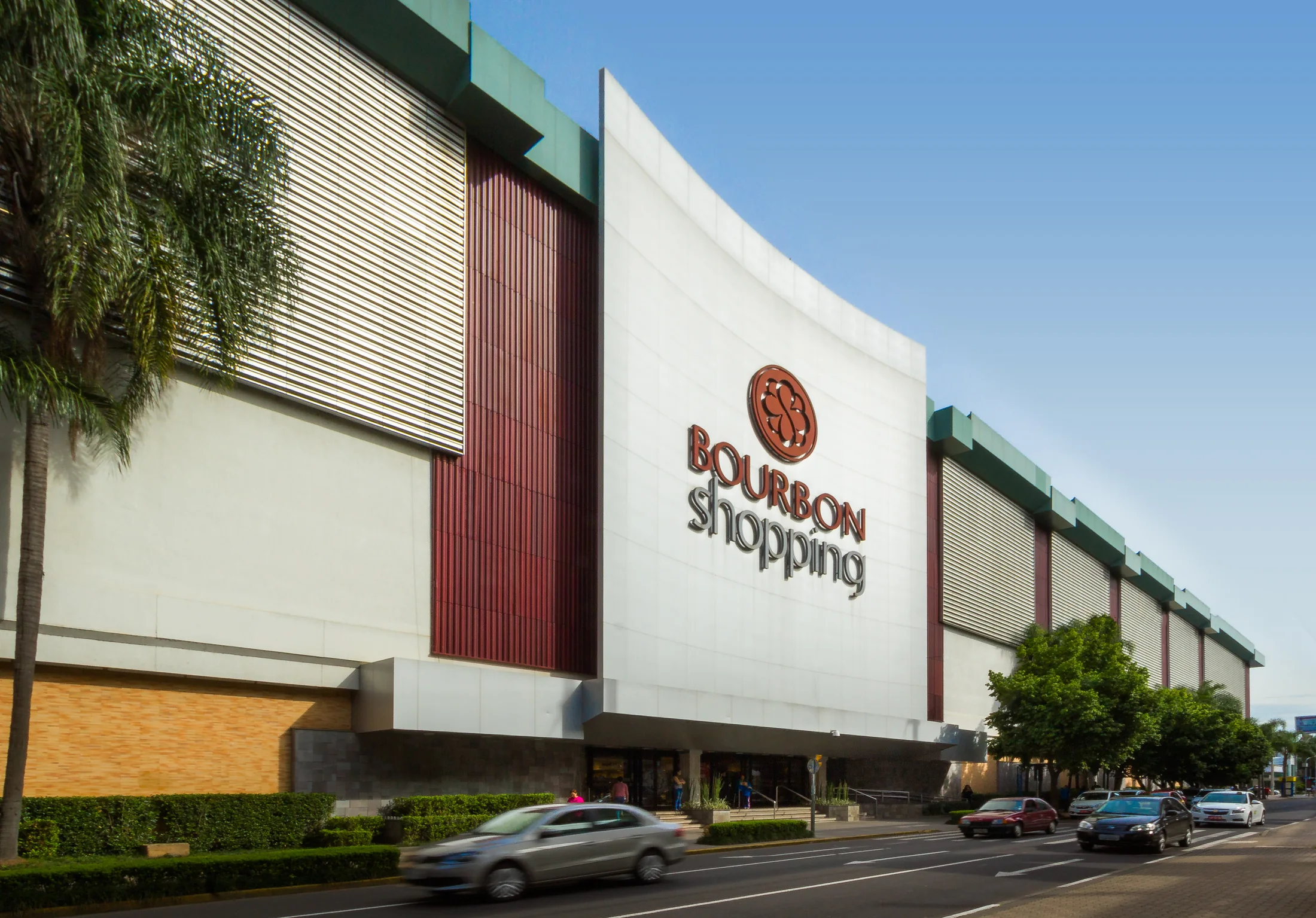 Fachada curva do Bourbon Shopping Novo Hamburgo, com o logotipo, painéis em vinho e faixas de metal, vista da rua.