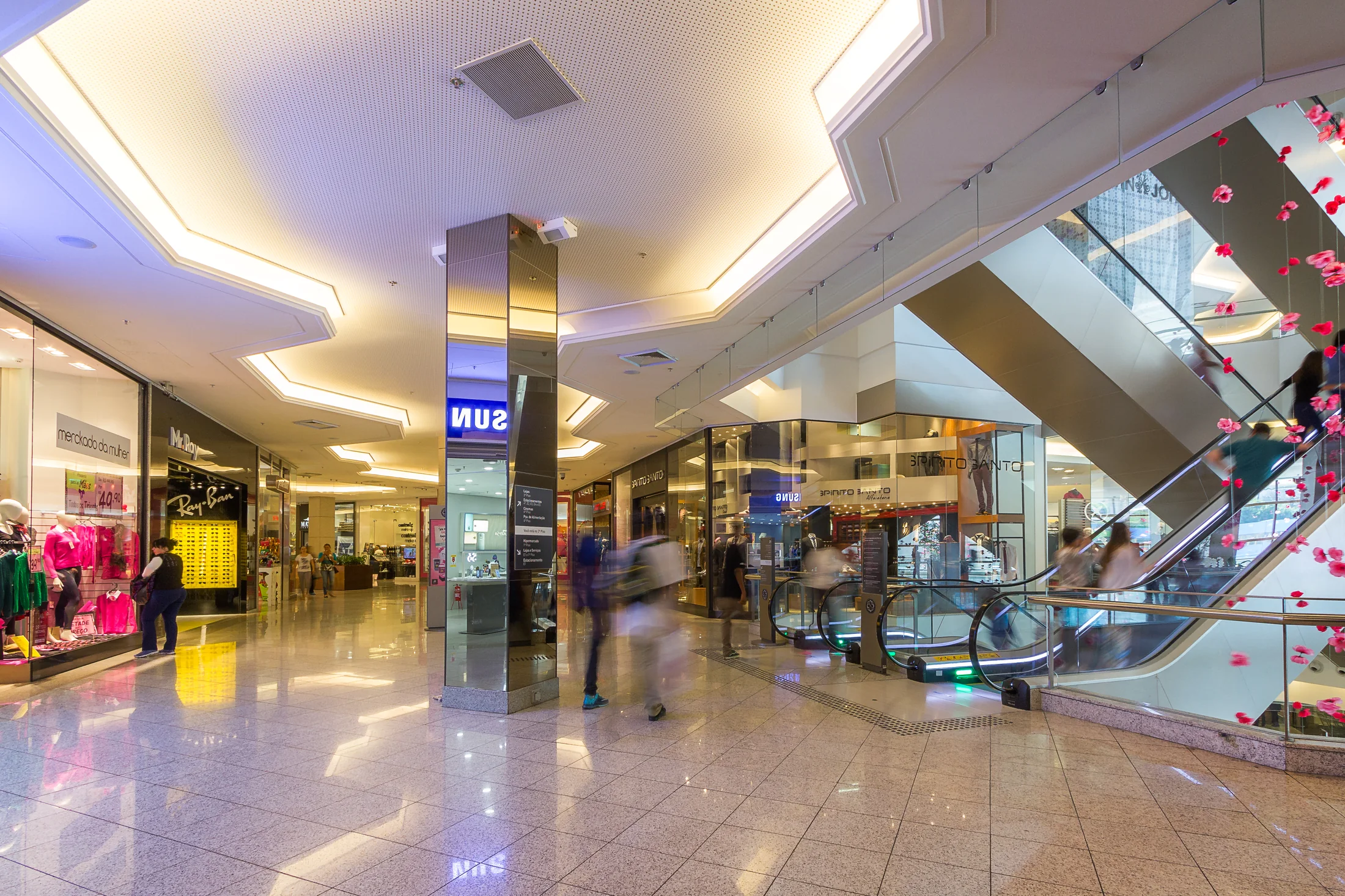 Galeria do Bourbon Shopping Wallig, com teto iluminado, pilar espelhado, escadas rolantes e pessoas em movimento.