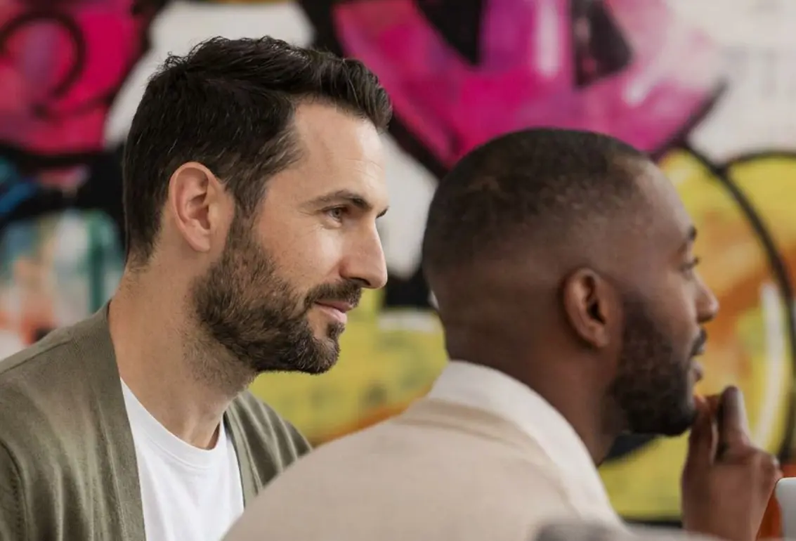 Dois homens de perfil diante de uma parede colorida de grafite.