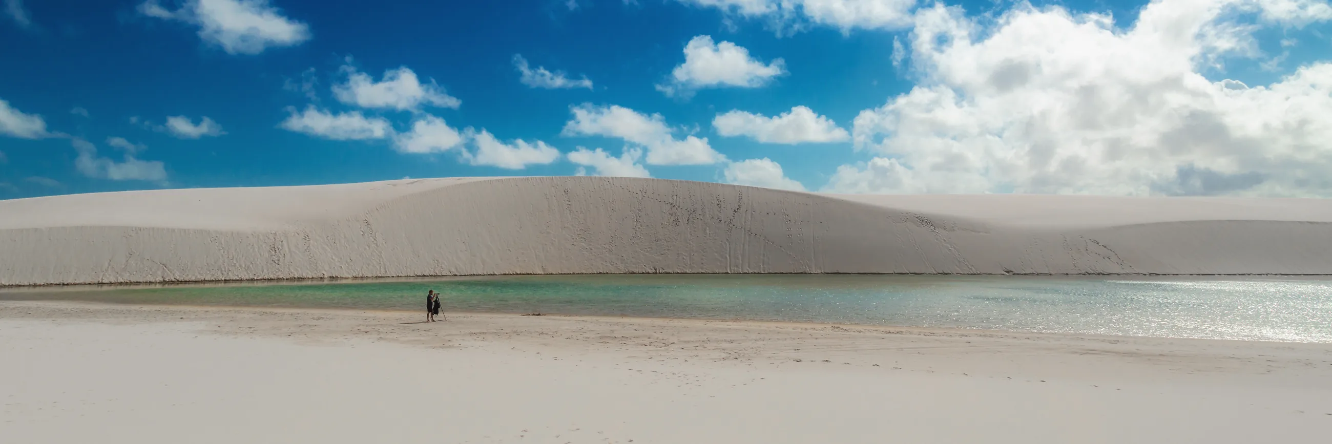 Uma pessoa sozinha numa grande duna branca, à beira de uma lagoa, nos Lençóis Maranhenses, perto de Atins.