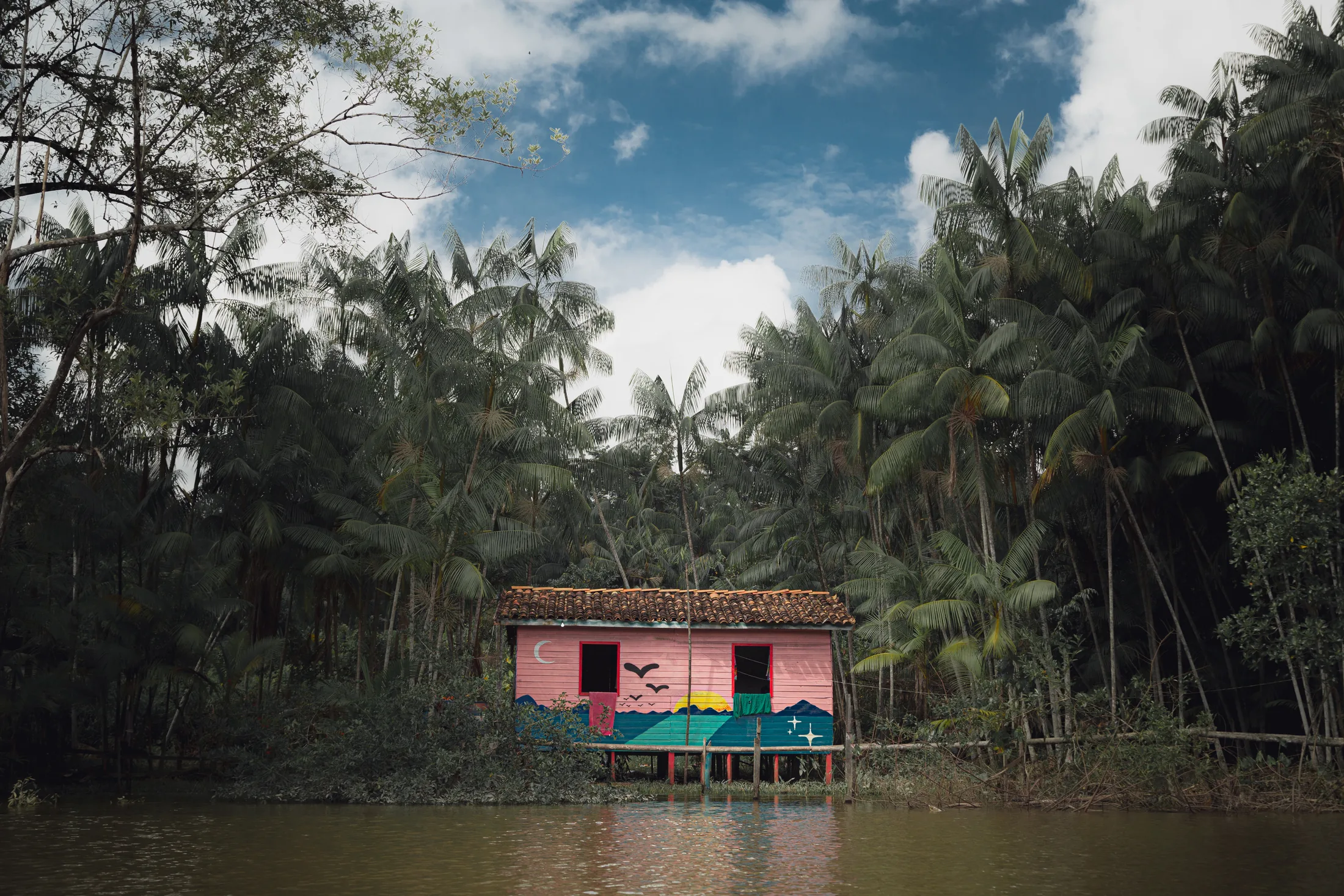 Uma casa colorida sobre palafitas, à beira de um rio, cercada de palmeiras, perto de Belém.