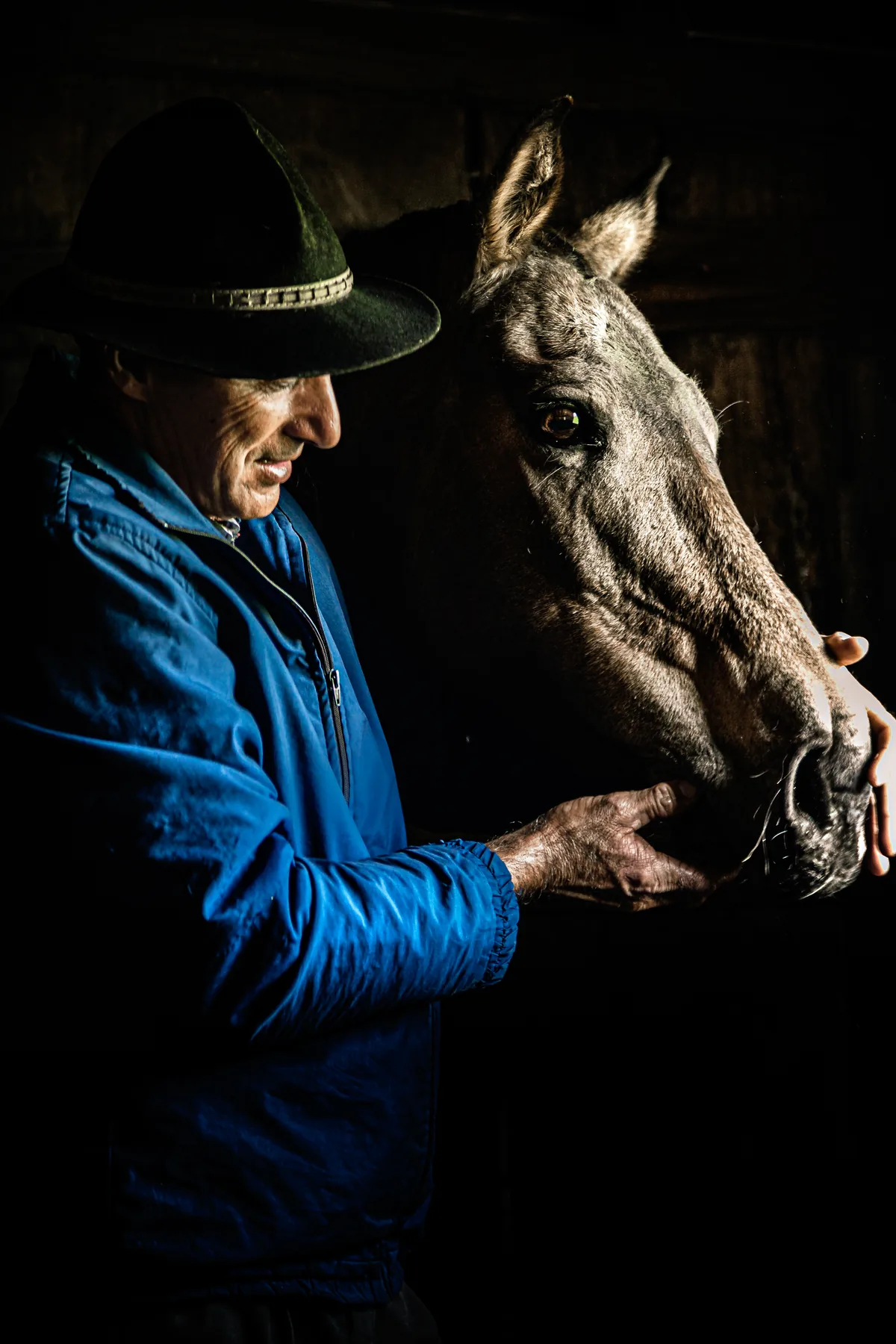 Retrato de um homem de casaco azul e chapéu ao lado de um cavalo, em Cambará do Sul.