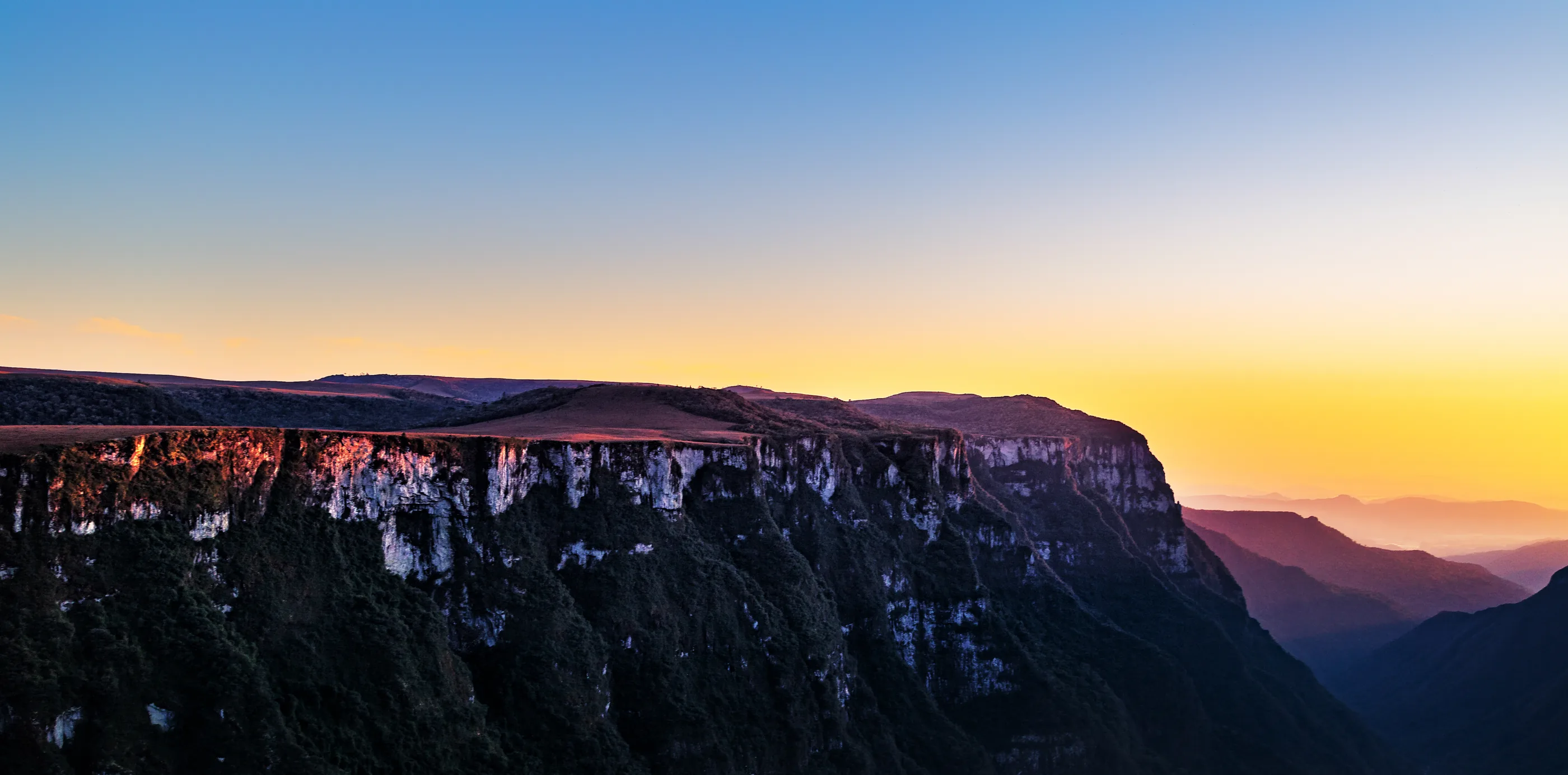 O Cânion Fortaleza ao pôr do sol, com o céu laranja e as paredes de rocha iluminadas.