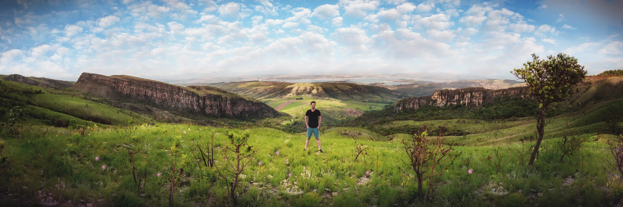 Panorâmica do Chapadão, com campos verdes, paredões de rocha e uma pessoa no centro, sob um céu com nuvens.