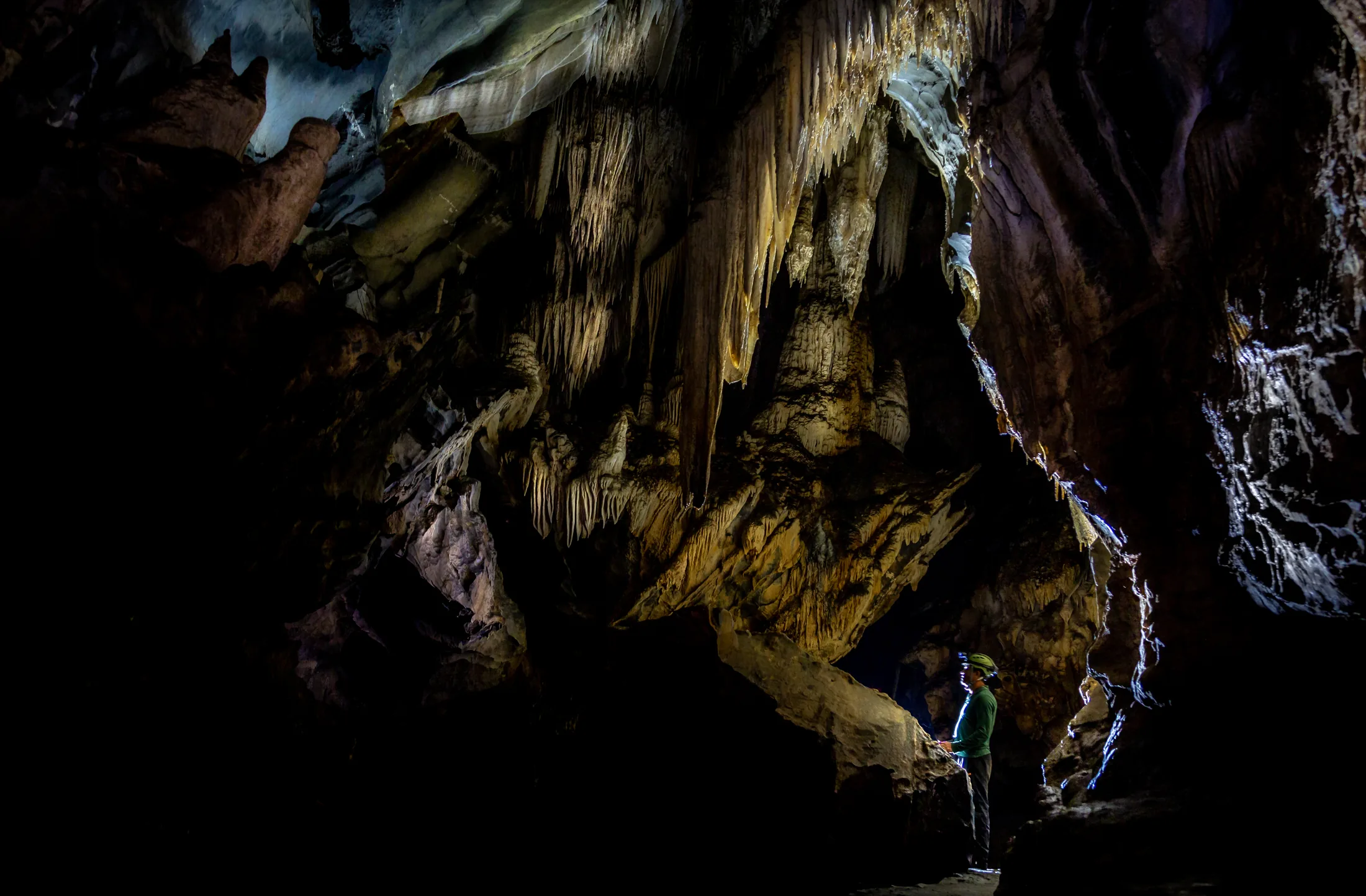 Interior de uma caverna em Iporanga, com formações de rocha iluminadas e uma pessoa pequena ao fundo.