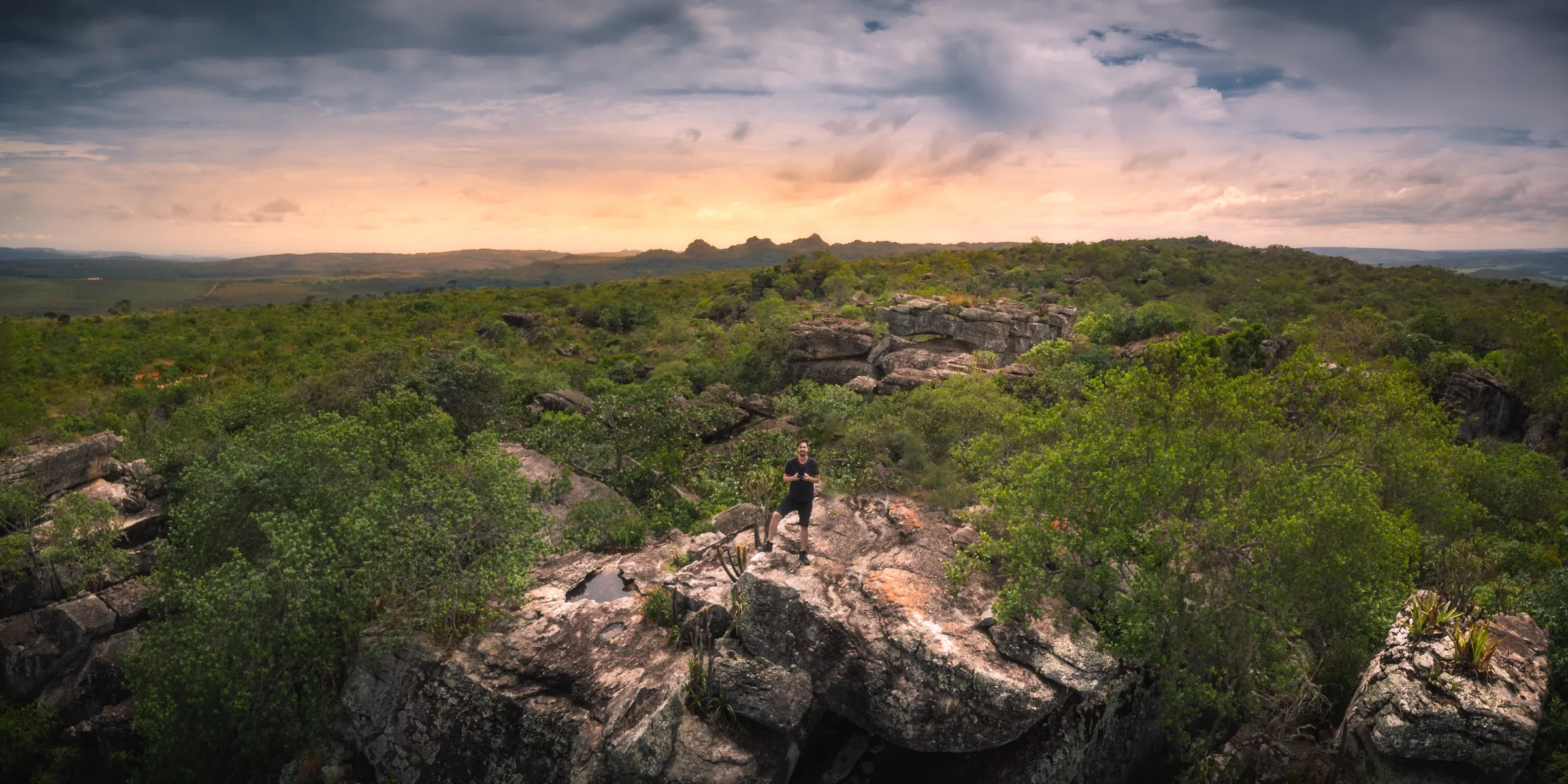 Paisagem do Parque dos Pirineus ao pôr do sol, com uma pessoa sobre as rochas, em meio à vegetação.